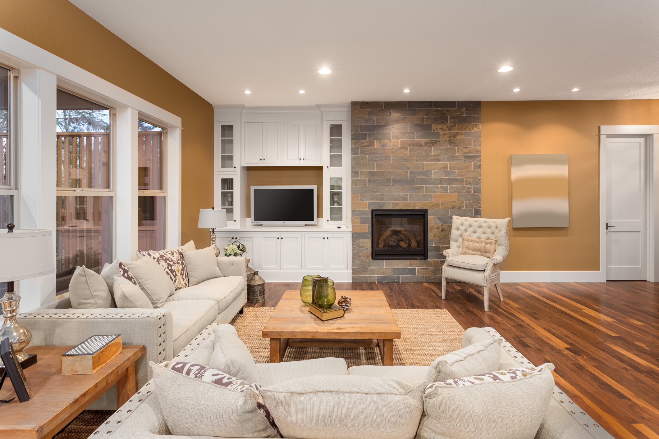 Beautiful living room interior with hardwood floors and fireplace in new luxury home. Two couches at right angles and pillows frame cozy family room with coffee table and built-in cabinets.